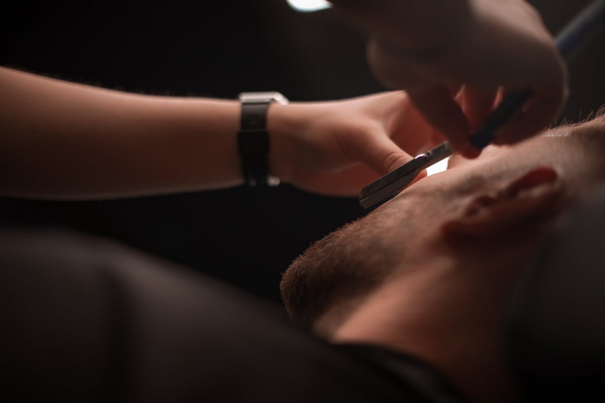 Barber shaving client's cheek with straight razor